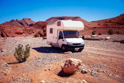 White camper van parked on a rocky desert landscape with red mountains and a clear blue sky.